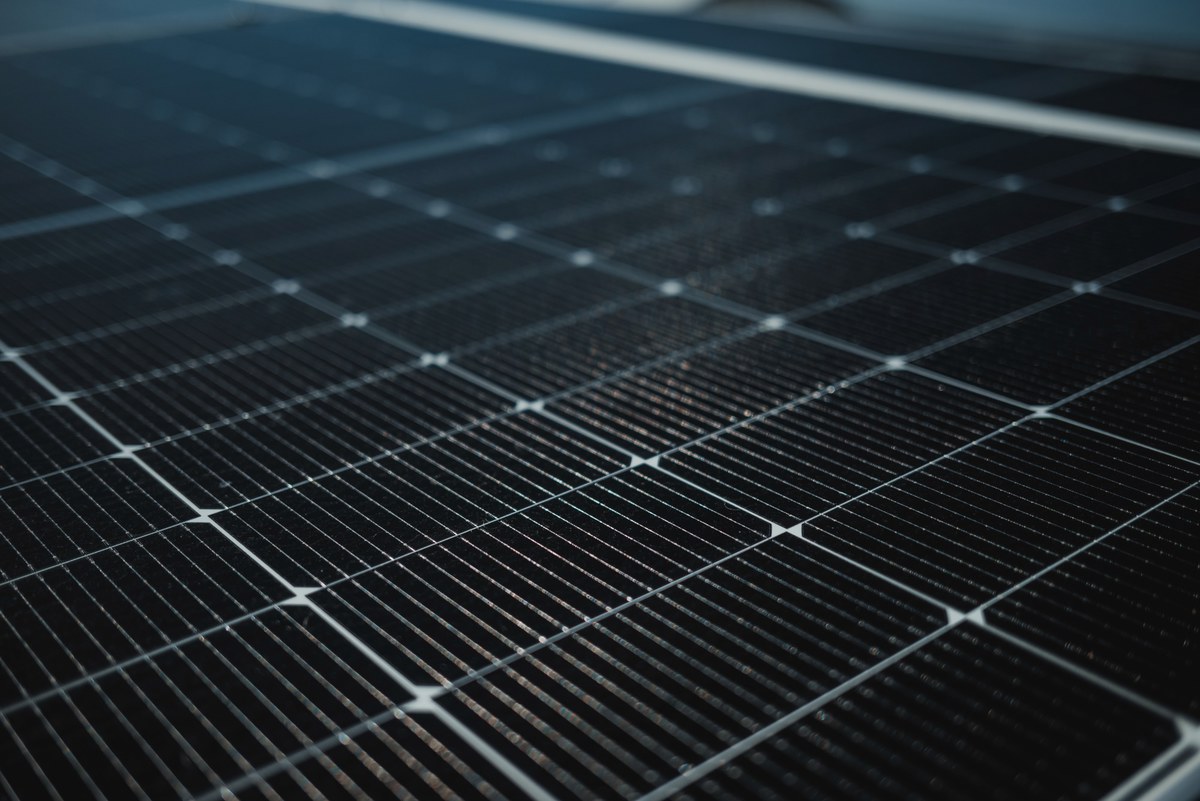 Close-up van donkere zonnepanelen met een raster van fijne zilvergrijze geleiderslijnen en cellen, scherp op de voorgrond en vervagend naar achteren.