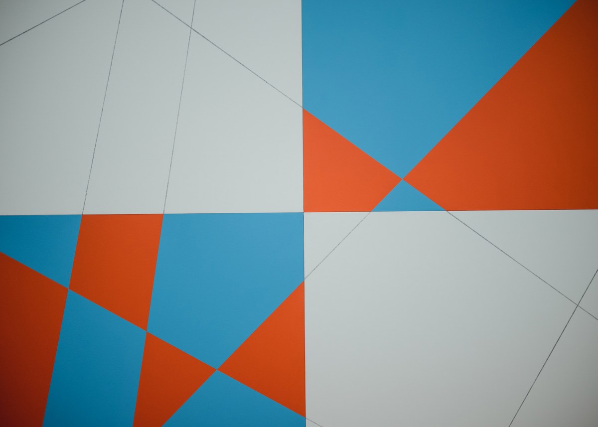 Geometrische compositie van driehoeken en vlakken in oranje, felblauw en lichtgrijs, doorsneden door dunne diagonale lijnen.