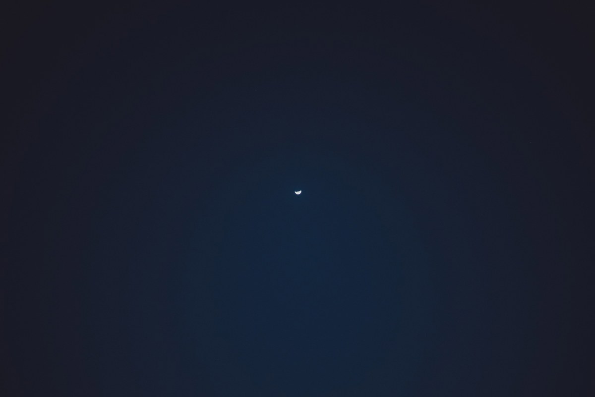 Een dunne sikkelmaan hangt als klein lichtpuntje midden aan een diepblauwe, bijna zwarte nachthemel boven Funchal.