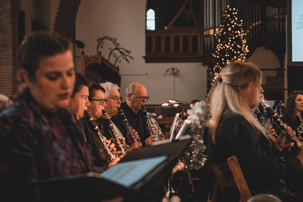 Klarinettisten spelen geconcentreerd van bladmuziek tijdens een kerstconcert in een kerk, met op de achtergrond een verlichte kerstboom en een orgel.