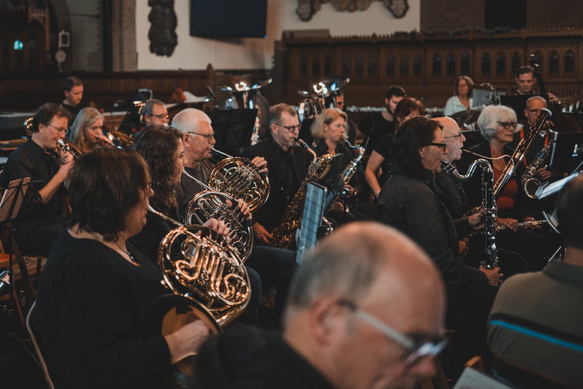 Musici van een blaasorkest spelen geconcentreerd op hoorn, saxofoon en klarinet tijdens een concert in een sfeervol verlichte kerk.