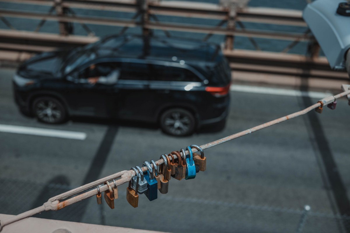 Een auto rijdt over de Brooklyn Bridge en we zien slotjes hangen aan een kabel.