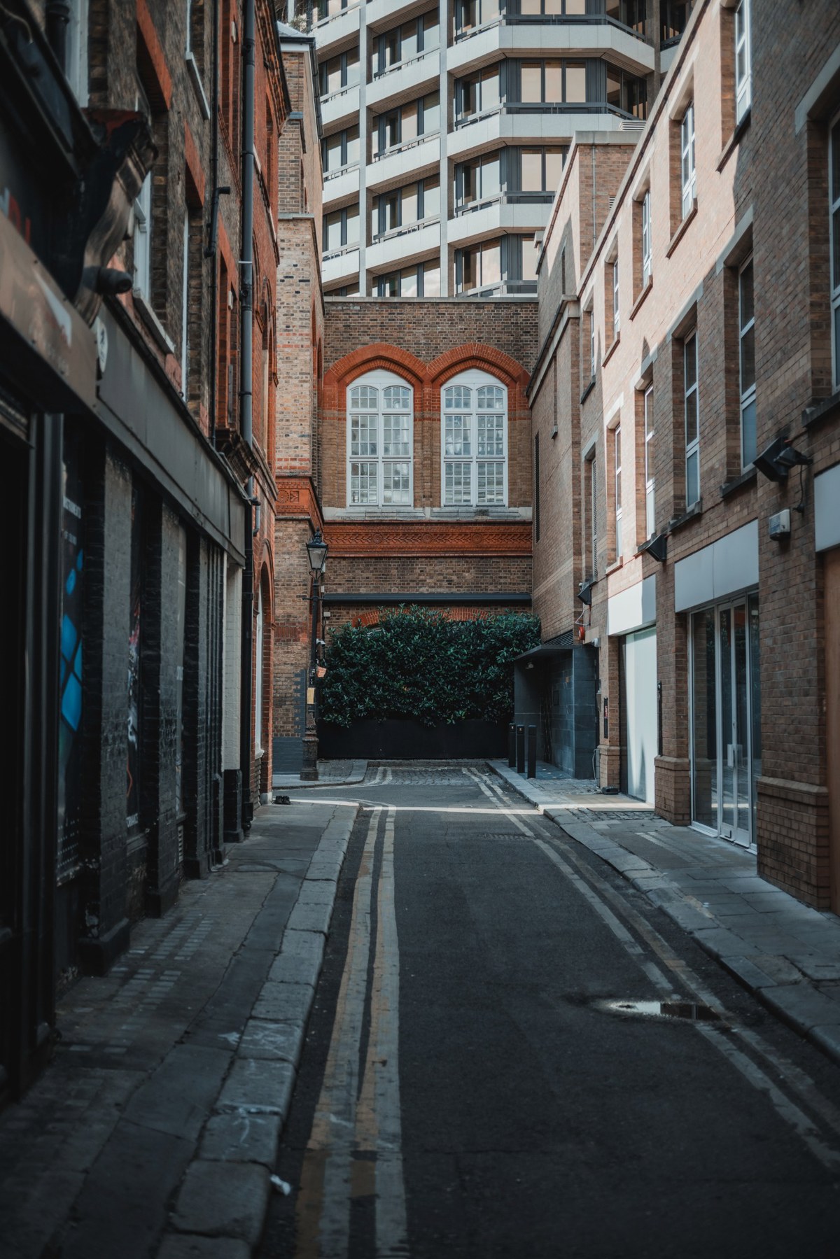 Een straatje in Londen waar de zon in valt. Achter de oude straat zien we een moderner flatgebouw.
