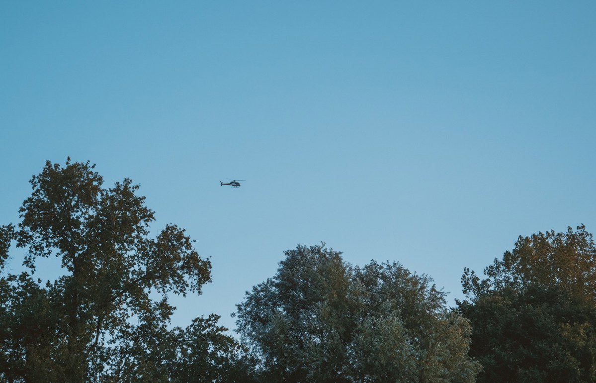 Een helikopter vliegt tegen een strakblauwe avondlucht boven de silhouetten van dichtbegroeide bomen tijdens de Amsterdam Marathon.