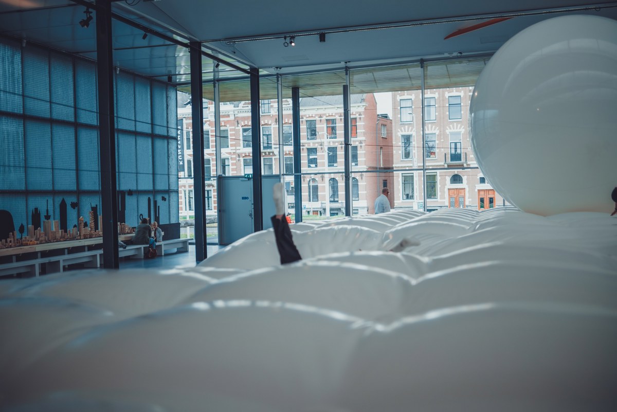 Bezoekers liggen op een groot wit opblaasbaar kunstwerk in de Kunsthal, met uitzicht door hoge ramen op historische bakstenen gevels.