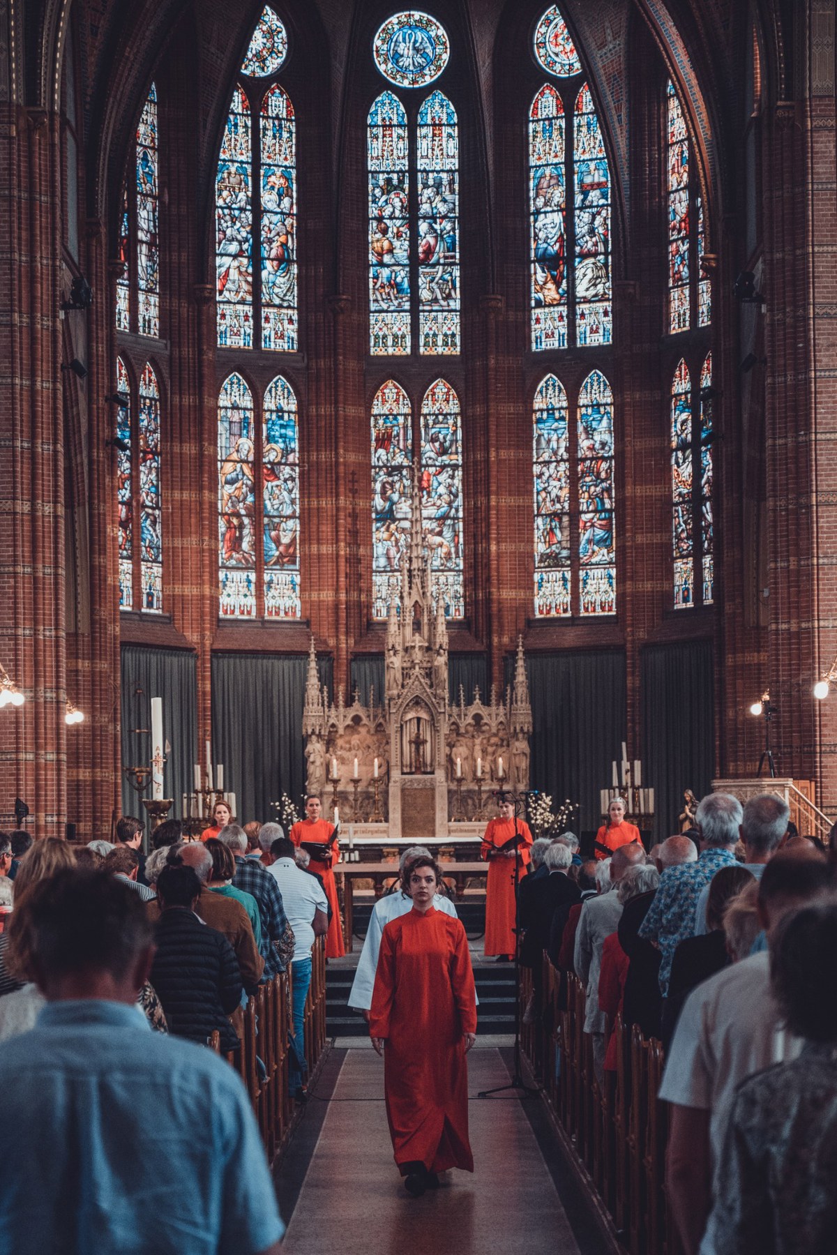 Herman Finkers en de zangeressen van Wishful Singing gefotografeerd. Ze lopen naar achteren door een volle kerk.
