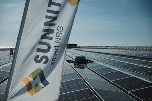 Een banner met het logo van Sunnit smart NRG wappert boven een groot dakveld vol zonnepanelen onder een strakblauwe lucht.