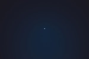 Een dunne sikkelmaan hangt als klein lichtpuntje midden aan een diepblauwe, bijna zwarte nachthemel boven Funchal.