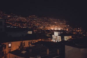 Vanaf een verhoogd standpunt kijk je 's nachts uit over de heuvels van Funchal, waar duizenden warme lichtjes tussen donkere huizen en daken glinsteren.