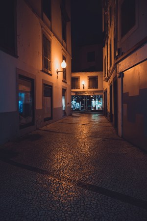 Een verlaten, met kinderkopjes geplaveide steeg 's nachts, verlicht door warme straatlantaarns, met aan het einde een winkel met etalagepoppen genaamd Casa Inglesa.