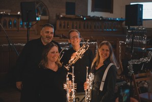 Vier lachende muzikanten poseren met glanzende trompetten in een sfeervol verlichte kerk tijdens een kerstconcert van KRPH.
