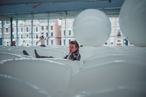 Bezoekers bewegen zich tussen grote witte opblaasbare kussens en ballen in een lichte kunstinstallatie met uitzicht op historische panden.