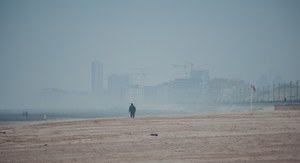 Een eenzame wandelaar loopt over een breed, mistig strand met op de achtergrond de vage skyline van de kuststad Middelkerke.