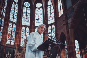 Herman Finkers in de kerk. Het glas in lood op de achtergrond.