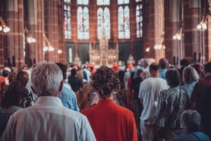 Herman Finkers en de zangeressen van Wishful Singing van achteren gefotografeerd. Ze lopen naar voren door een volle kerk.