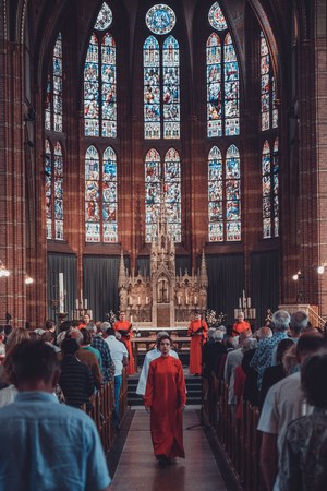 Herman Finkers en de zangeressen van Wishful Singing gefotografeerd. Ze lopen naar achteren door een volle kerk.