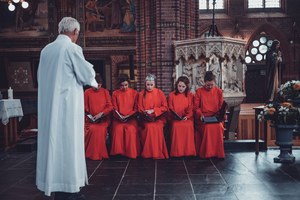 Herman Finkers spreekt de zangeressen van Wishful Singing aan. Zij zitten samen naast elkaar op een bank.