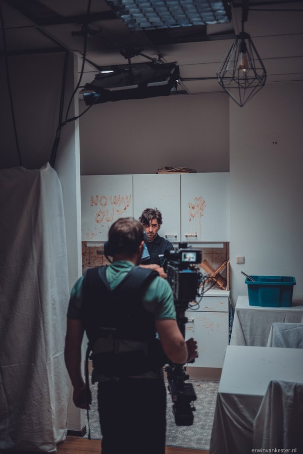 Cameraman met steadicam filmt een acteur voor een kast met de bloederige tekst NO WAY OUT tijdens de opnames van een horrorfilm.