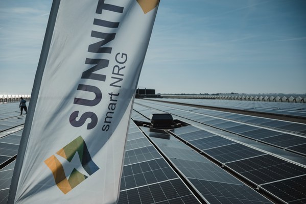 Een banner met het logo van Sunnit smart NRG wappert boven een groot dakveld vol zonnepanelen onder een strakblauwe lucht.