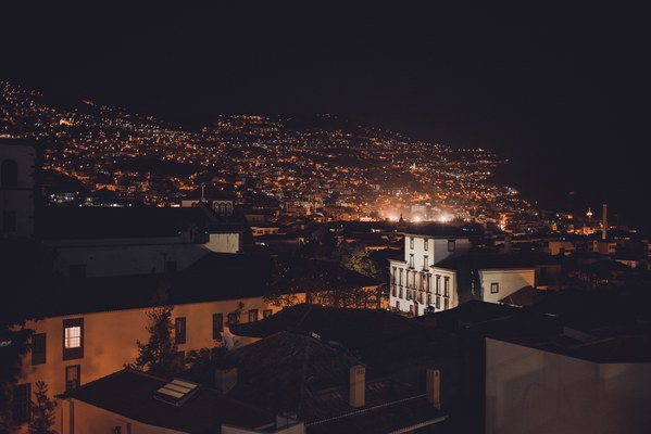 Vanaf een verhoogd standpunt kijk je 's nachts uit over de heuvels van Funchal, waar duizenden warme lichtjes tussen donkere huizen en daken glinsteren.