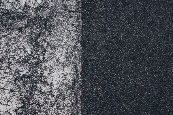 Verweerde witte wegmarkering vervaagt op donker asfalt, waar de afgesleten verf overgaat in het onbeschilderde, korrelige wegdek.