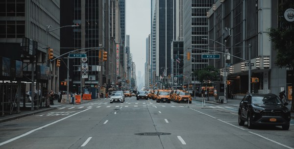 Een drukke straat in New York. We kijken de diepte in langs wolkenkrabbers, auto's en taxi's.