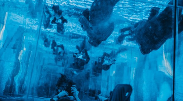 Bezoekers kijken van onderaf omhoog door een blauw verlicht wateroppervlak waarop mensen lijken te lopen, in een spiegelende installatie in de Kunsthal.