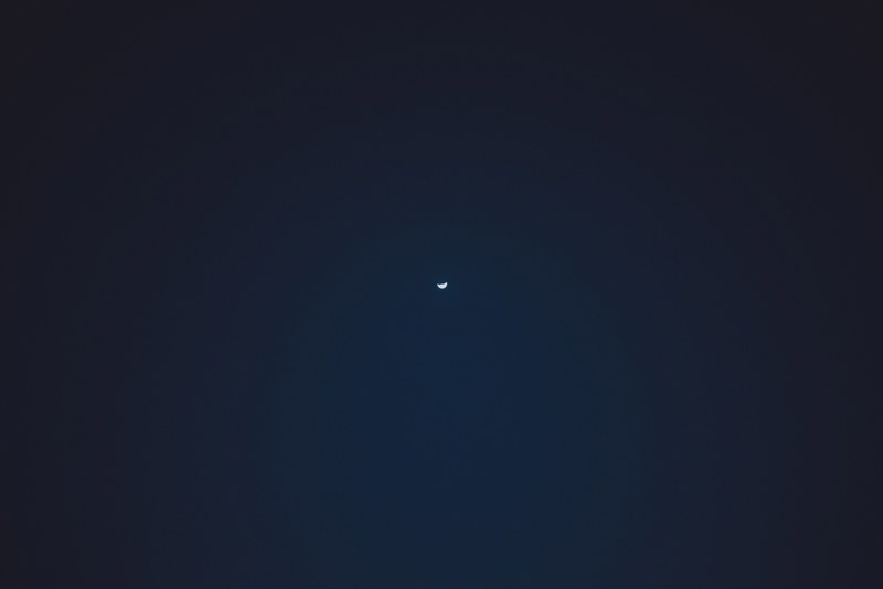 Een dunne sikkelmaan hangt als klein lichtpuntje midden aan een diepblauwe, bijna zwarte nachthemel boven Funchal.