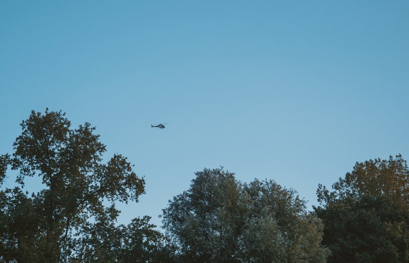 Een helikopter vliegt tegen een strakblauwe avondlucht boven de silhouetten van dichtbegroeide bomen tijdens de Amsterdam Marathon.