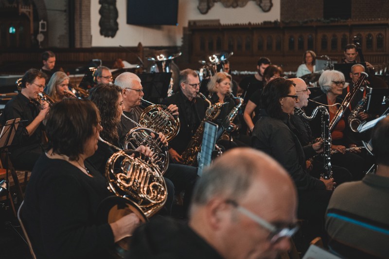 Musici van een blaasorkest spelen geconcentreerd op hoorn, saxofoon en klarinet tijdens een concert in een sfeervol verlichte kerk.