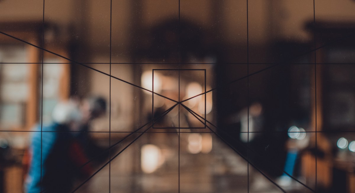 Wazig interieur van het Teylers Museum gezien door een glaswand met geometrische lijnen, met vaag zichtbare bezoekers en warme lichten op de achtergrond.