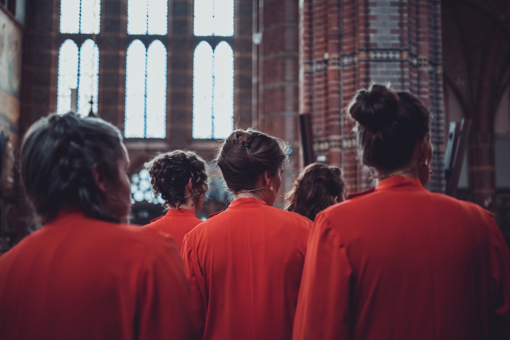 De zangeressen van Wishful Singing van achteren gefotografeerd. Ze kijken allemaal naar rechts.